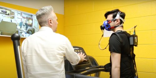 Student talks to research participant who is walking on treadmill while wearing mask apparatus